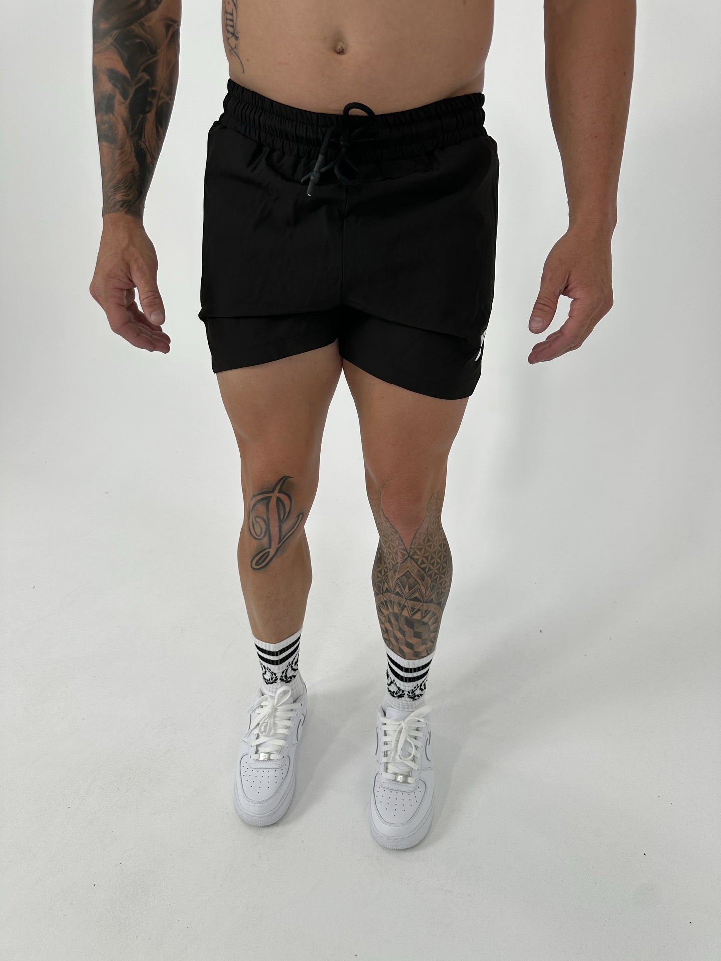 Person wearing black shorts and white sneakers on a plain background